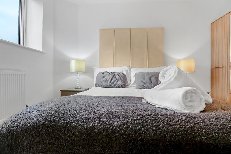 Modern bedroom with double bed, upholstered headboard, bedside lamps and wooden wardrobe