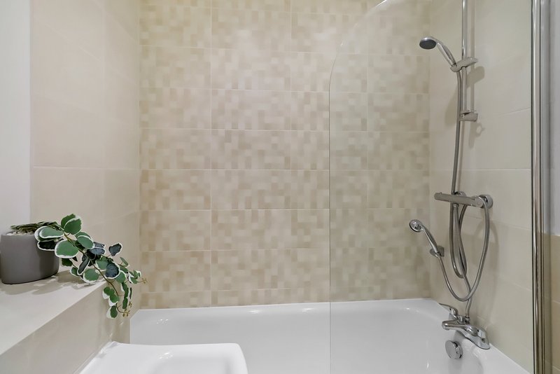 Modern bathroom with bathtub, glass shower screen, tiled walls and potted plant