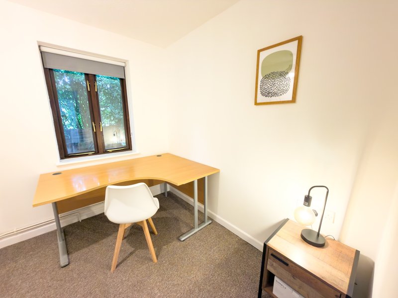 Bright home office with wooden desk, white chair, window, and framed wall art