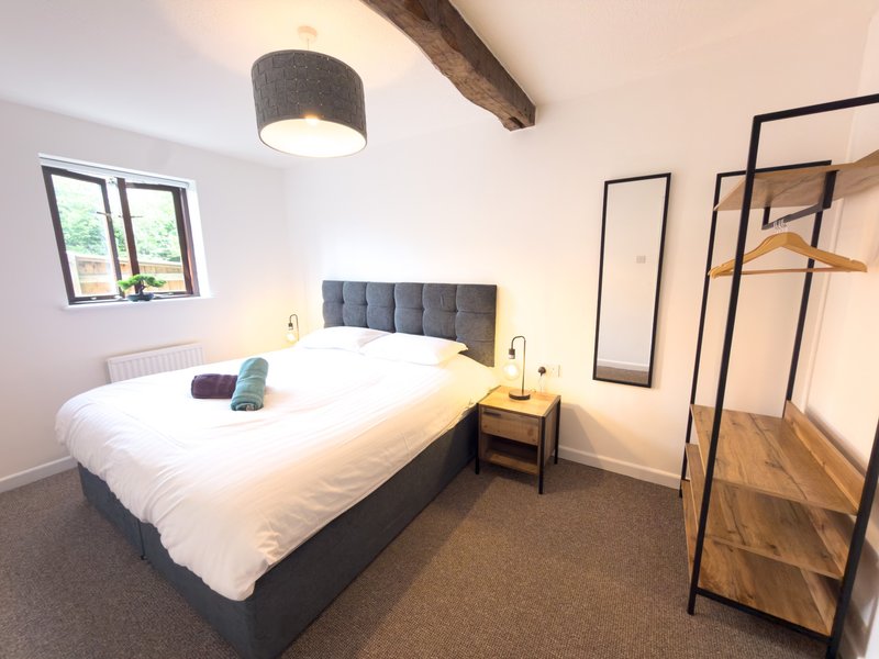 Modern bedroom with double bed, gray headboard, wooden beams, and clothing rack