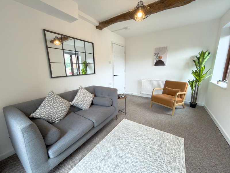 Spacious living room with grey sofa, mid-century chair, wooden beams and potted plants