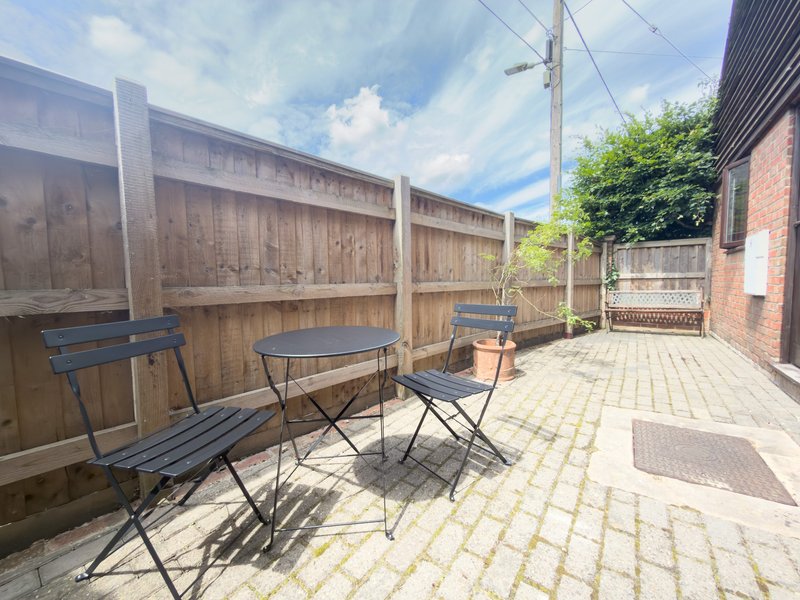 Paved outdoor patio with wooden fence, garden furniture, and brick building