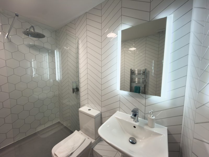 Modern bathroom with hexagonal tile walls, walk-in shower, illuminated mirror and white fixtures
