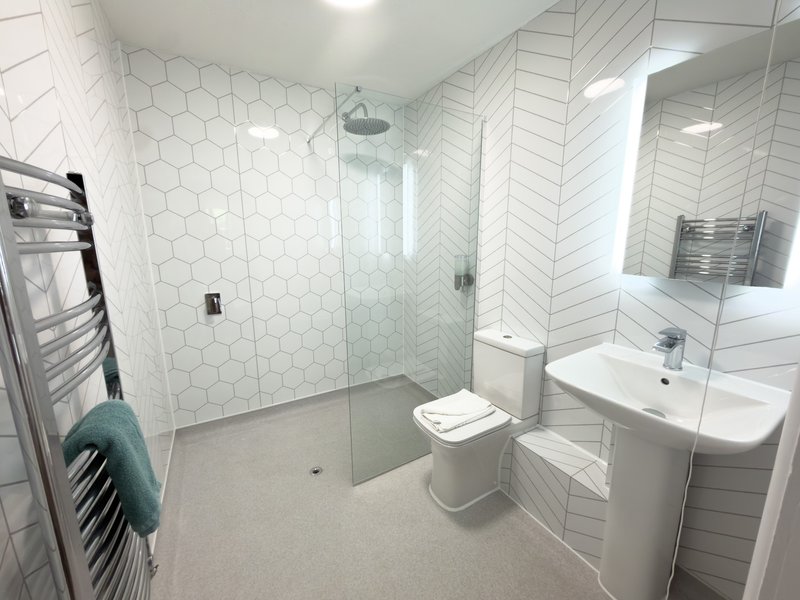 Modern bathroom with walk-in shower, white tile walls, toilet, sink and heated towel rail