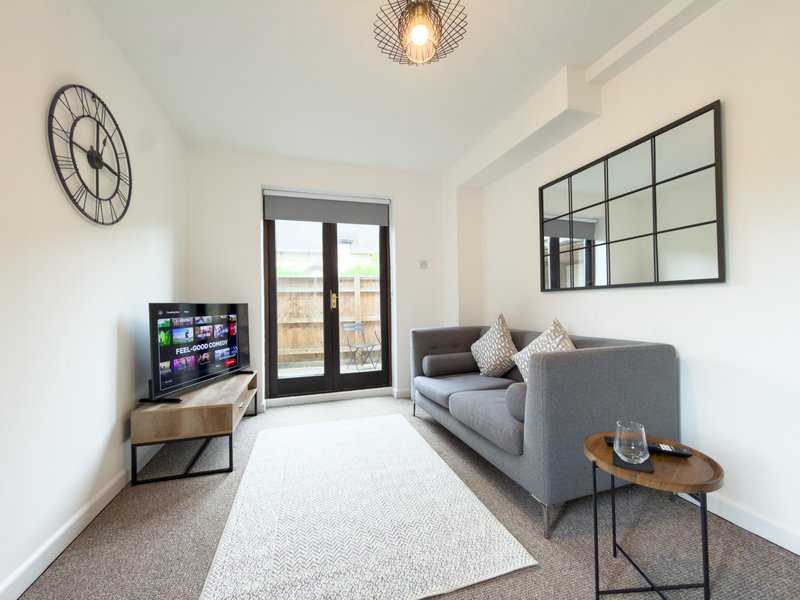 Modern living room with gray sofa, TV, wall clock, grid mirror and glass doors to balcony