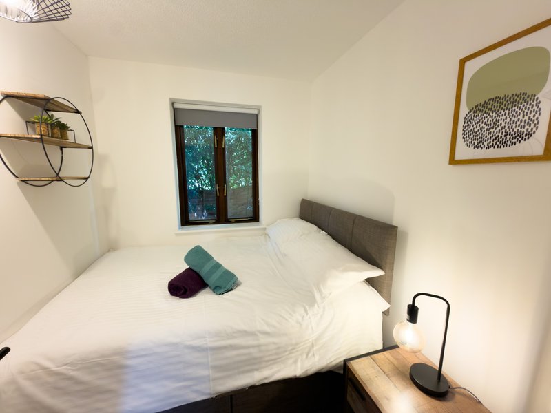 Compact bedroom with double bed, white bedding, dark headboard and window view