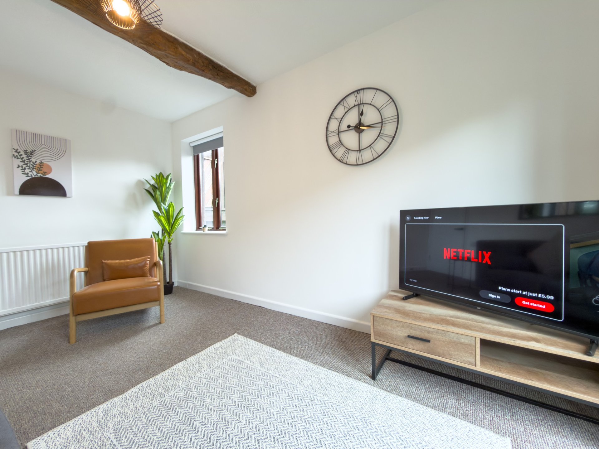 Modern living room with TV, wooden beam ceiling, mustard armchair and wall clock