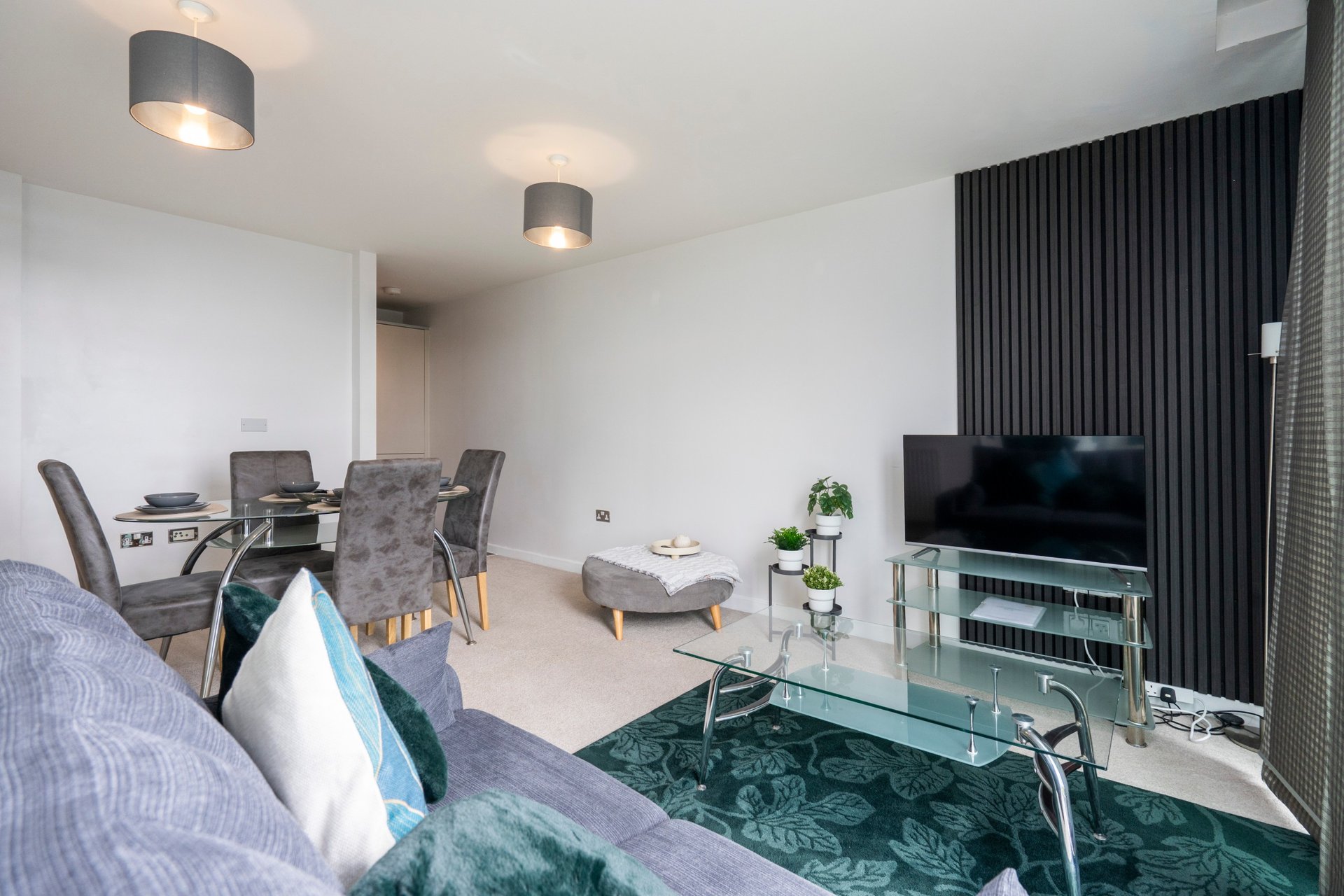 Modern open-plan living room with sofa, dining table, TV stand and contemporary lighting fixtures