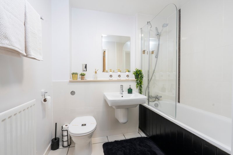 Modern bathroom with white tiles, pedestal sink, toilet, bathtub and shower screen