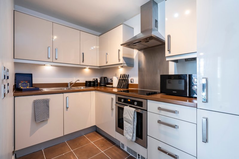 Modern kitchen with white cabinetry, stainless steel appliances, and brown tile flooring