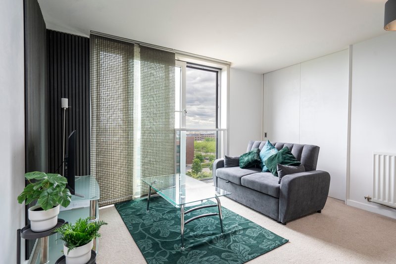 Modern living room with gray sofa, green rug, potted plants, and floor-to-ceiling windows overlooking garden