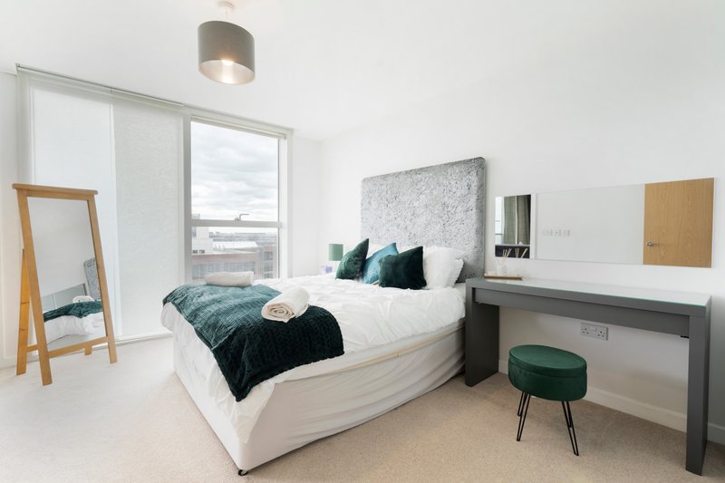 Modern bedroom with double bed, teal and black bedding, desk, mirror and pendant light