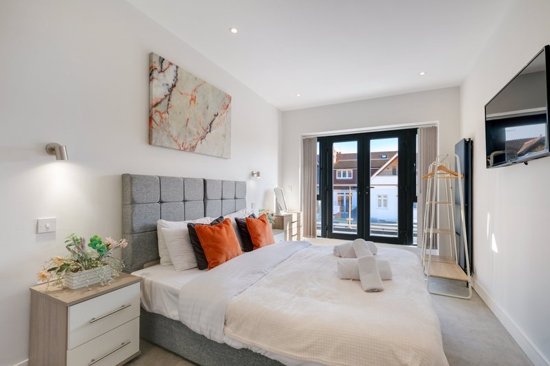 Modern bedroom with gray upholstered bed, orange pillows, white bedding, and balcony doors