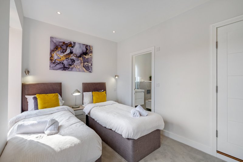 Twin bedroom with two single beds, brown headboards, yellow cushions, wall art and ensuite access
