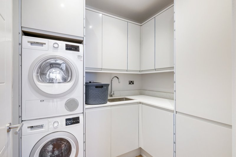 Laundry room with stacked white washing machines, sink, and white cabinetry storage