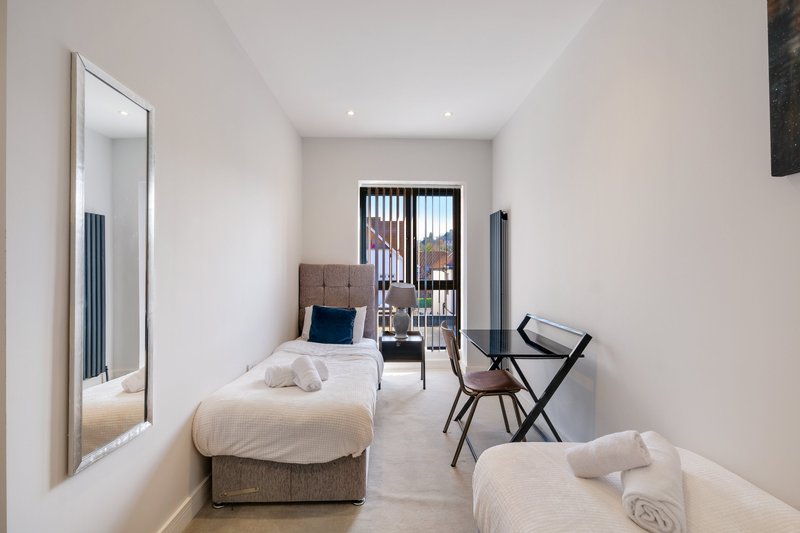 Modern twin bedroom with two single beds, large mirror, desk chair and city views through balcony doors
