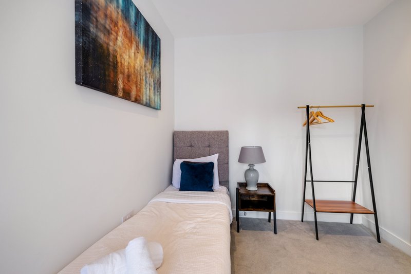 Compact bedroom with single bed, grey headboard, bedside table, floor lamp and clothing rack