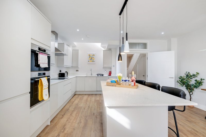 Modern white kitchen with island, built-in appliances, wooden flooring and pendant lighting