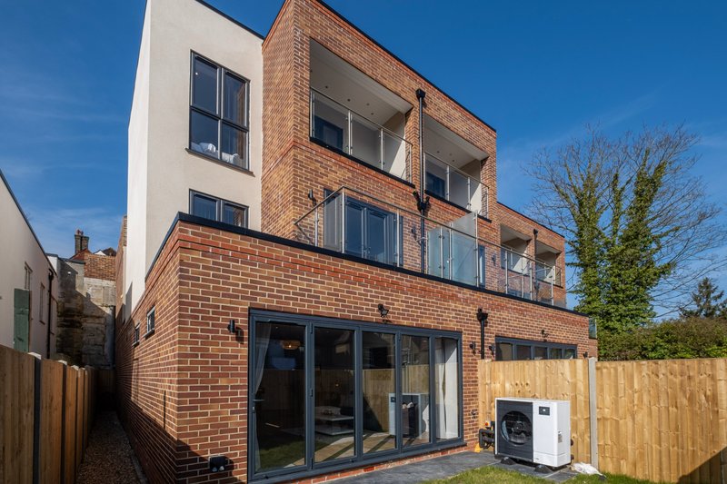 Modern brick house exterior with large windows, wooden fence and clear sky view