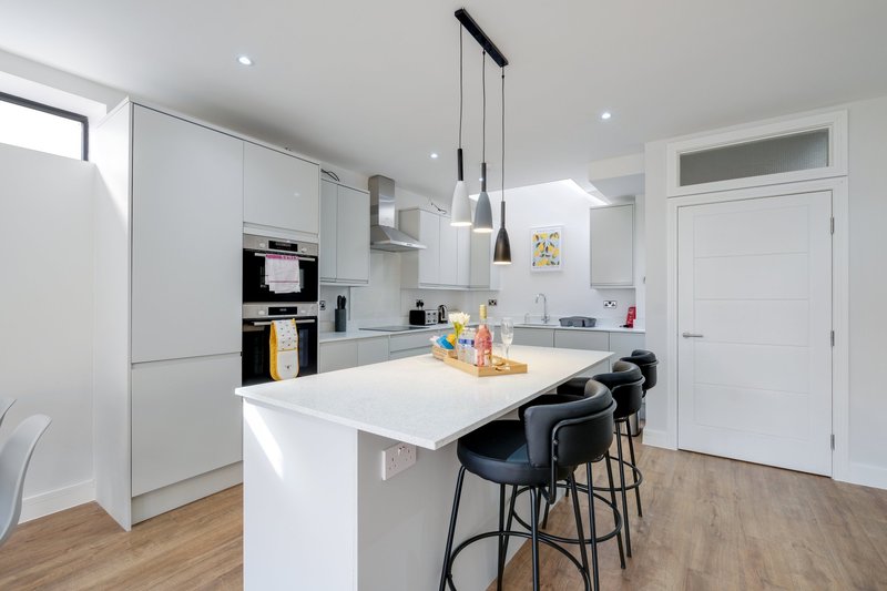 Modern white kitchen with island, bar seating, built-in appliances and pendant lighting