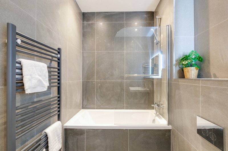 Modern bathroom with tiled shower enclosure, built-in bathtub, heated towel rail and potted plant
