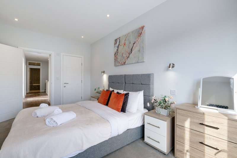 Modern bedroom with double bed, gray headboard, orange cushions, white bedding and wooden furniture