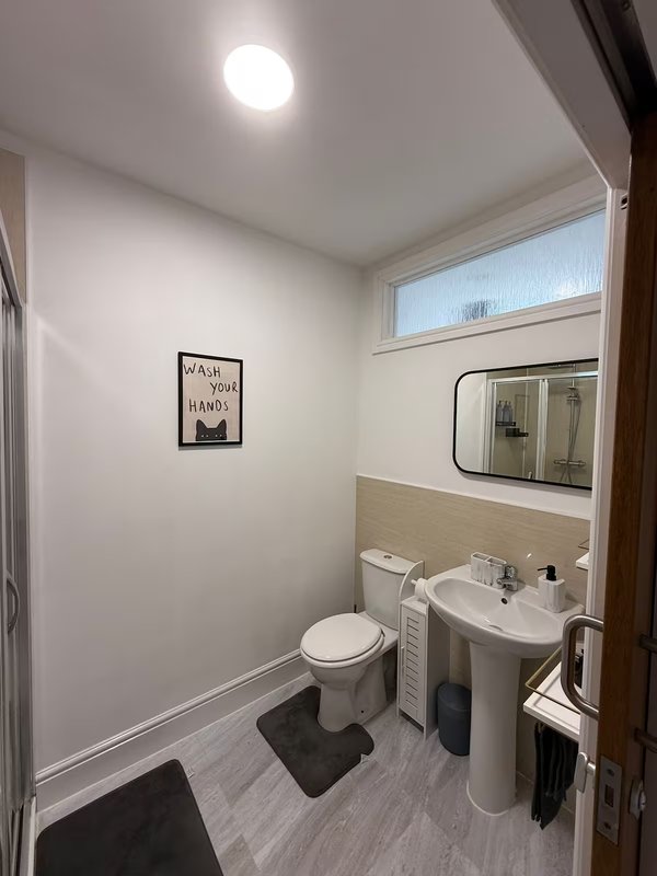 Clean bathroom with toilet, pedestal sink, mirror and small window