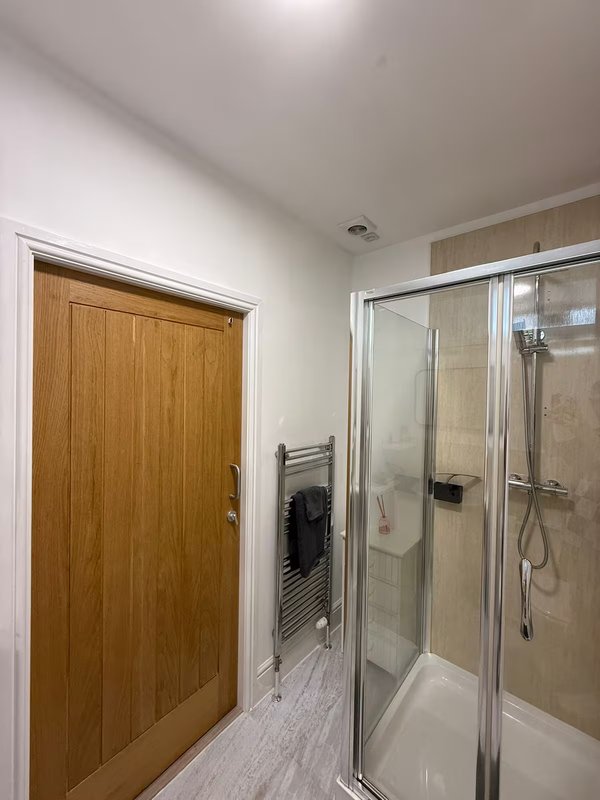 Modern bathroom with shower enclosure, wooden door, and light tile flooring