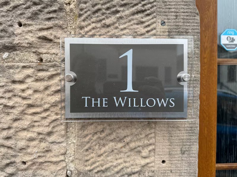 Modern house number plaque mounted on stone exterior wall