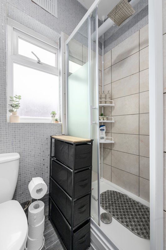 Compact bathroom with toilet, black storage unit, shower enclosure and tiled walls