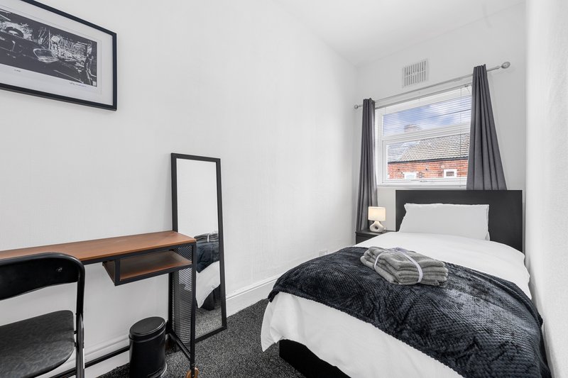Compact bedroom with single bed, desk, mirror and window overlooking brick buildings