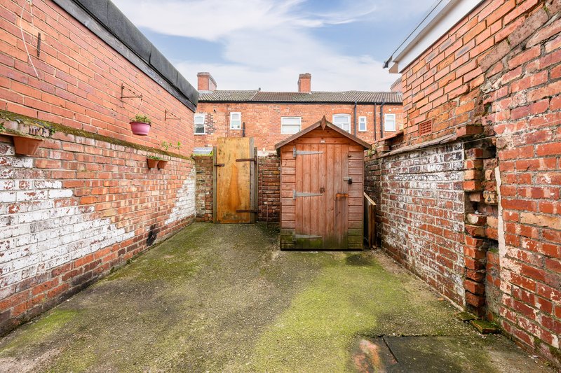 Brick-walled courtyard with wooden doors, moss-covered ground, and period buildings