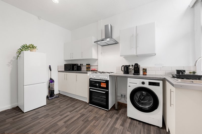 Modern kitchen with white cabinets, integrated appliances, washing machine and wooden floor