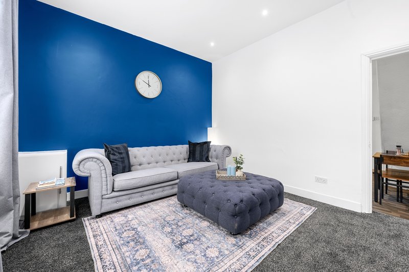 Modern living room with blue accent wall, grey sofa, dark ottoman, and wall clock