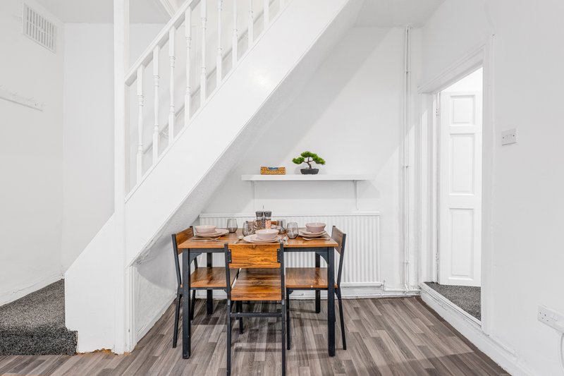 Modern dining area under staircase with wooden table, black chairs and white shelving