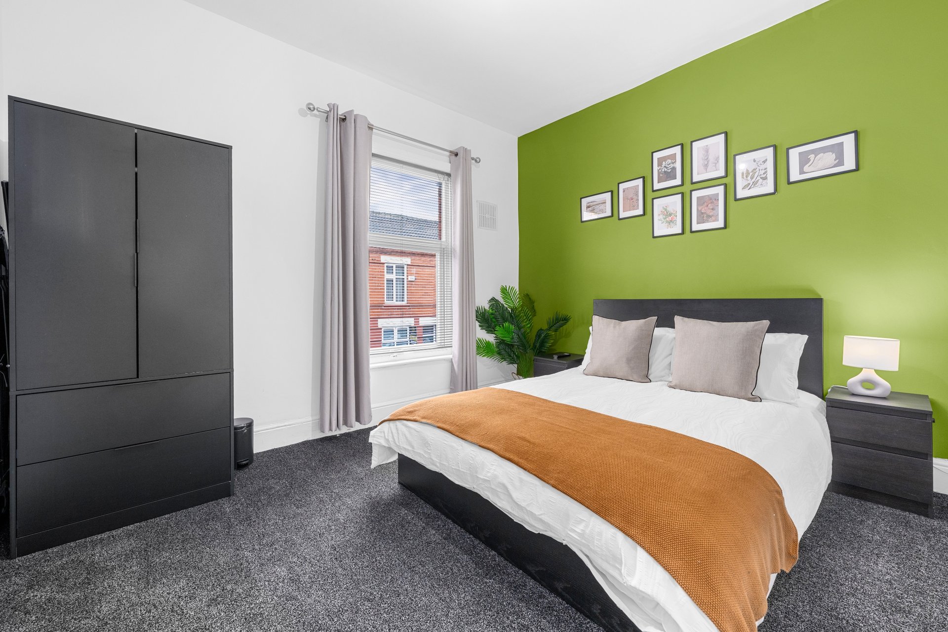 Bright bedroom with double bed, orange throw, green accent wall, black wardrobe and window view