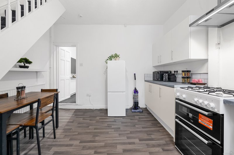 Modern open-plan kitchen and dining area with white cabinetry, gas range, dining table and stairs