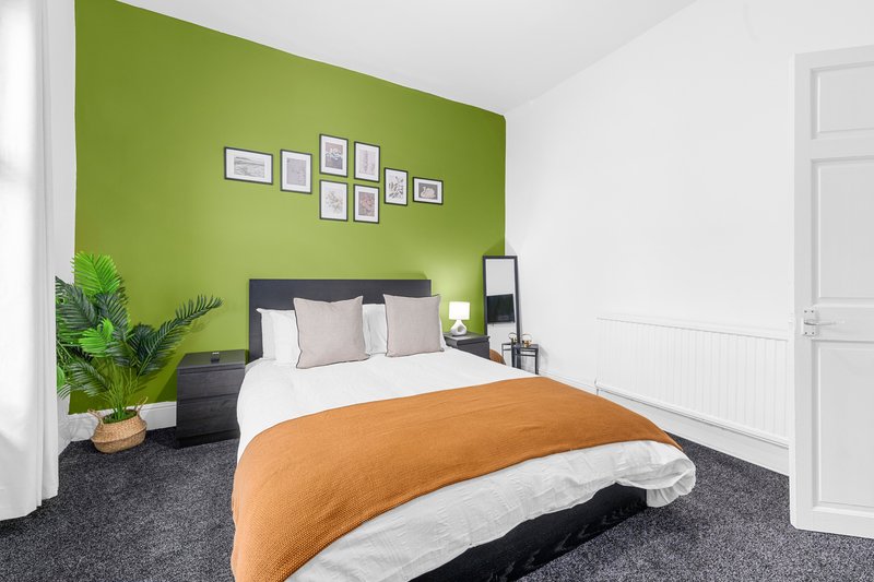 Bedroom with bright green accent wall, double bed with orange throw, potted plant and framed artwork