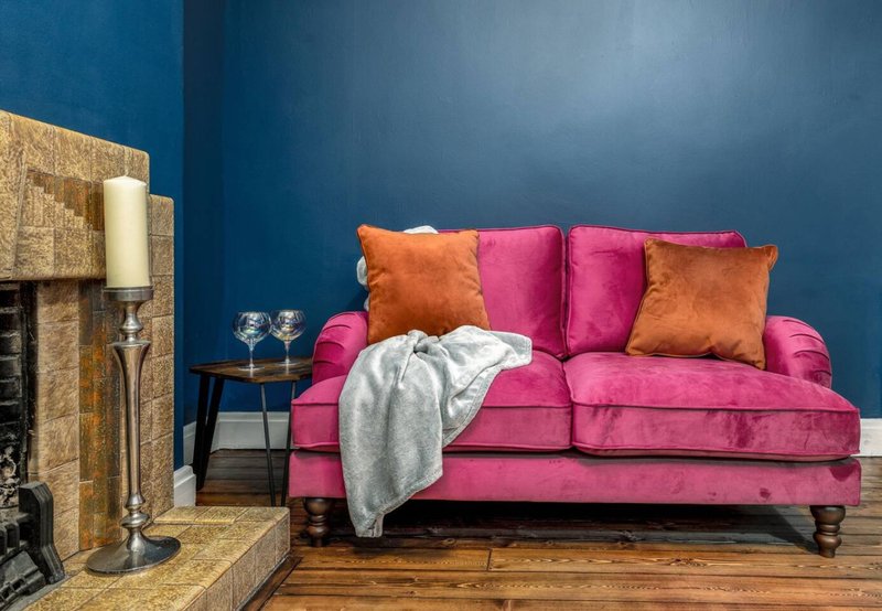 Living room with pink velvet sofa, orange and magenta cushions, fireplace, and blue accent wall