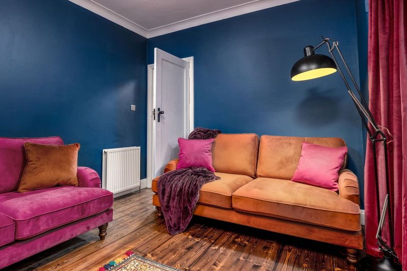 Living room with colorful sofas, blue walls, wooden floor and arc lamp