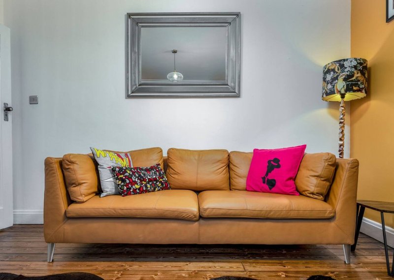 Tan leather sofa with colorful cushions in modern living room with wood flooring