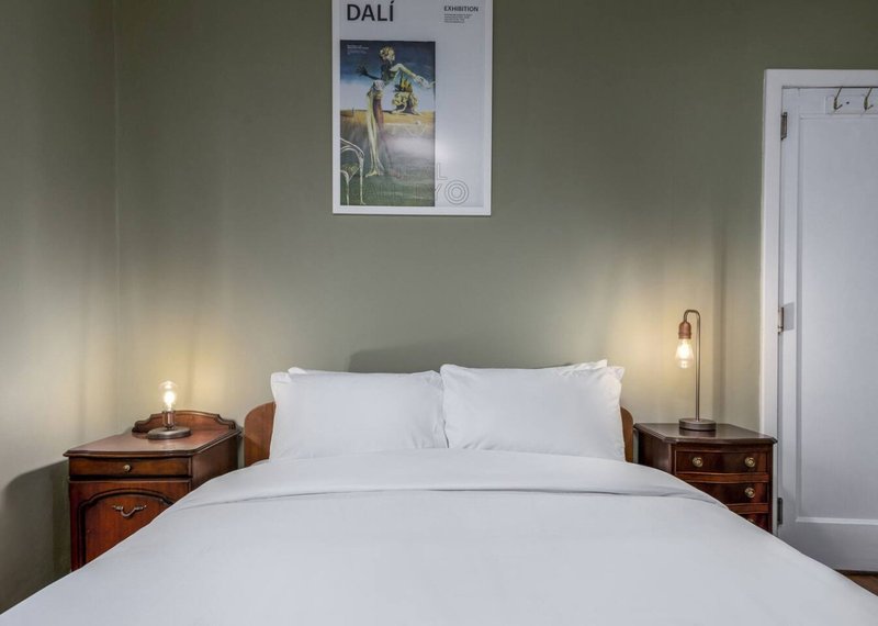 Bedroom with white bedding, wooden nightstands, pendant lamps, and wall art