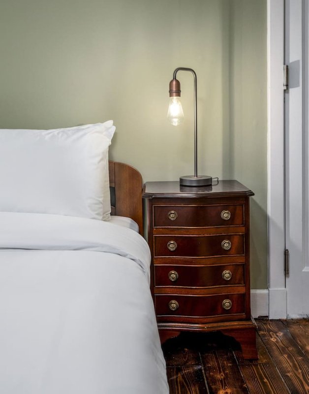 Bedroom with white bedding, wooden bedside table, brass-handled drawers, and pendant lamp