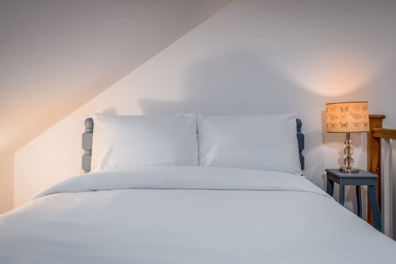 Bright attic bedroom with white bedding, pillows, wooden headboard and side lamp