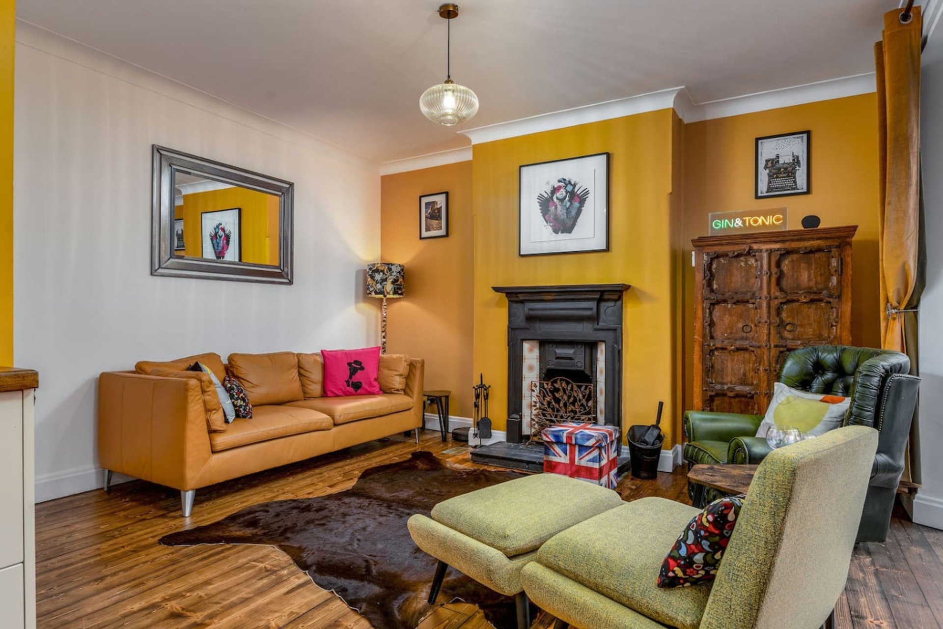 Warm living room with mustard walls, orange sofa, fireplace, and green armchairs