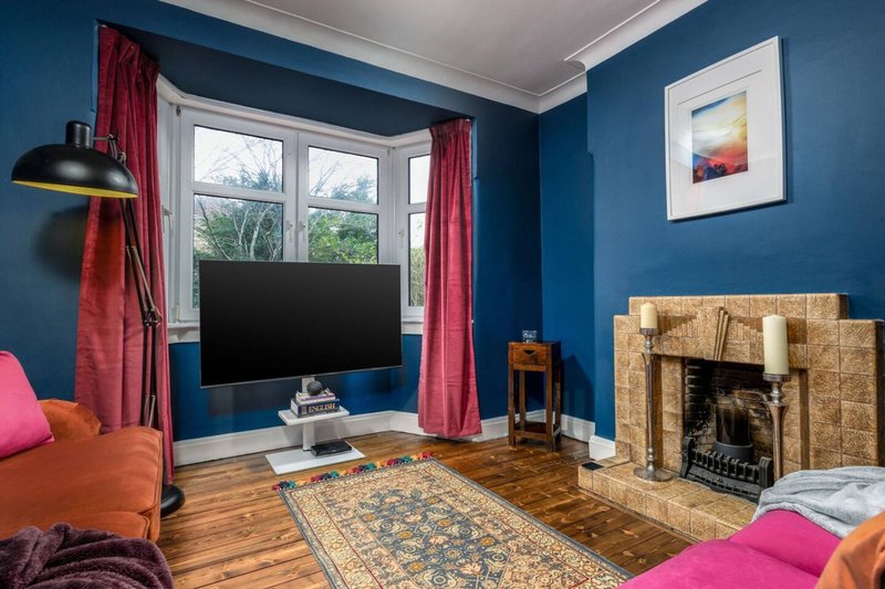 Living room with blue walls, fireplace, TV, orange sofa and pink cushions