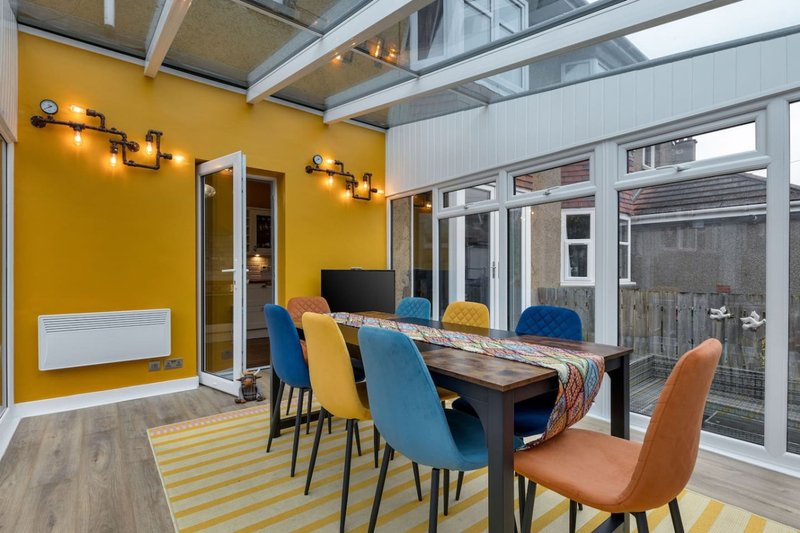 Modern dining area with colorful chairs, wooden table, yellow walls and glass doors to garden