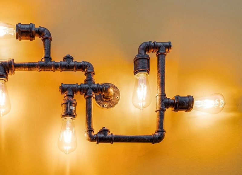 Industrial-style pipe fixture with exposed bulbs mounted on yellow wall