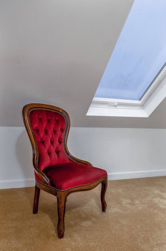 Attic bedroom with red velvet chair, skylight window, and carpeted floor
