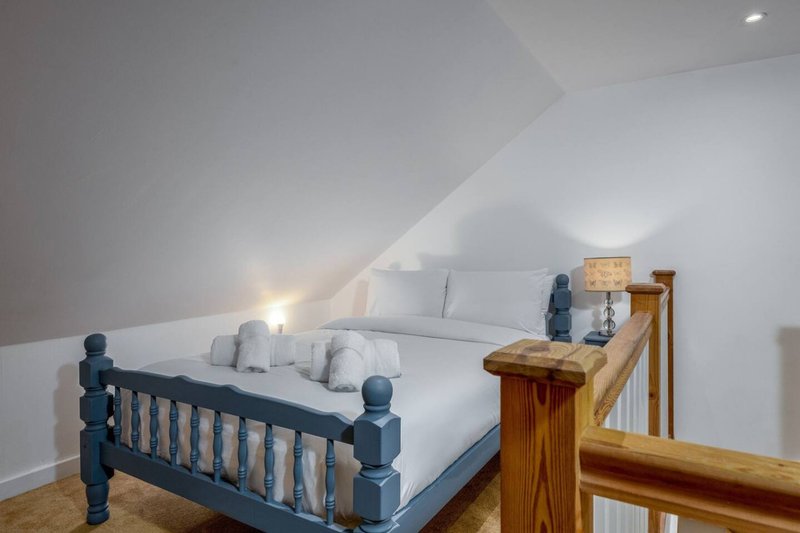 Attic bedroom with double bed, wooden frame, sloped ceiling and bedside lamp